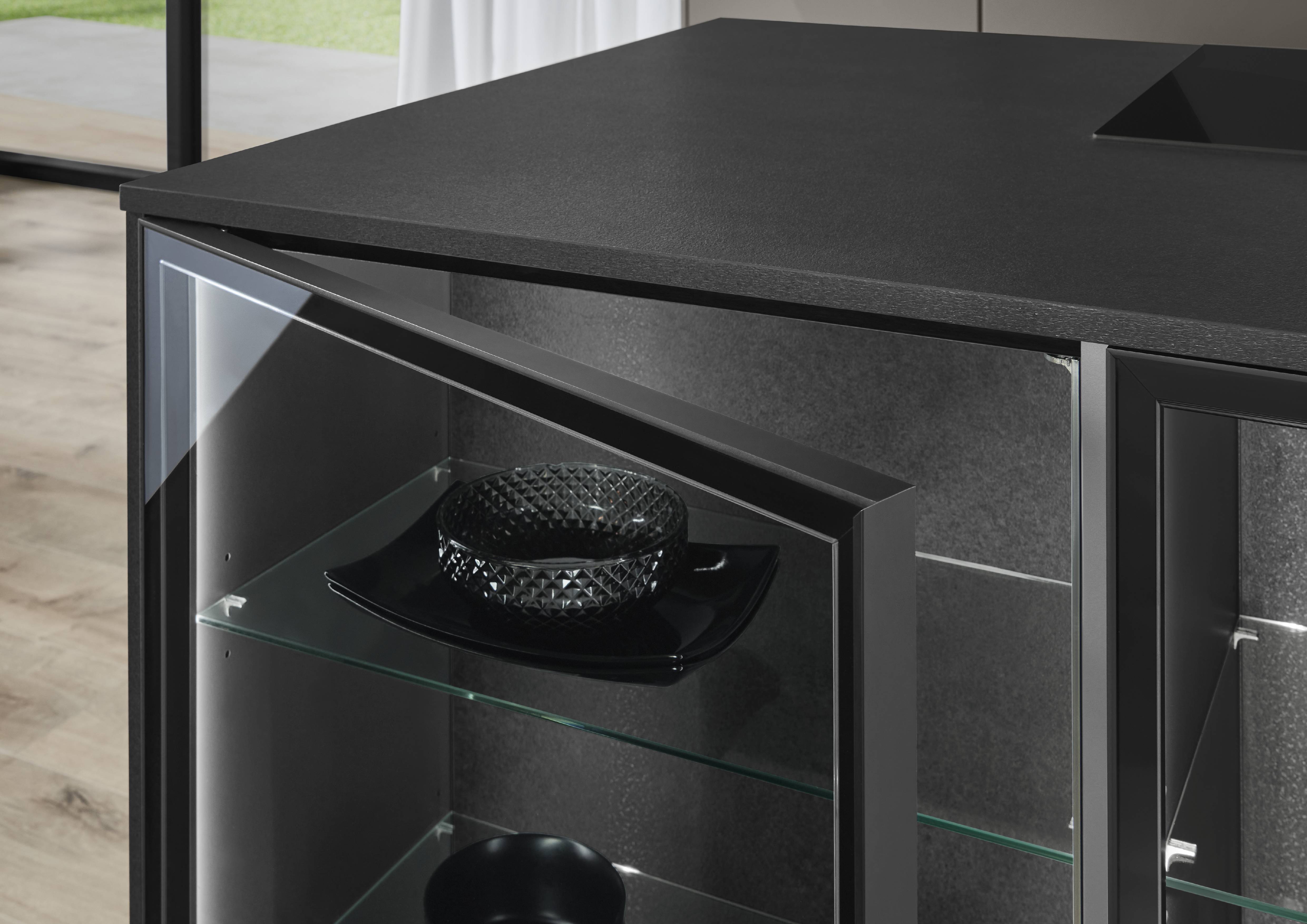 Novalux Kitchen — Anthracite with Illuminated Glass Display Cabinet Close-up of a dark anthracite kitchen unit with an open glass display cabinet revealing backlit shelves holding black decorative bowls, paired with a matte black textured countertop.