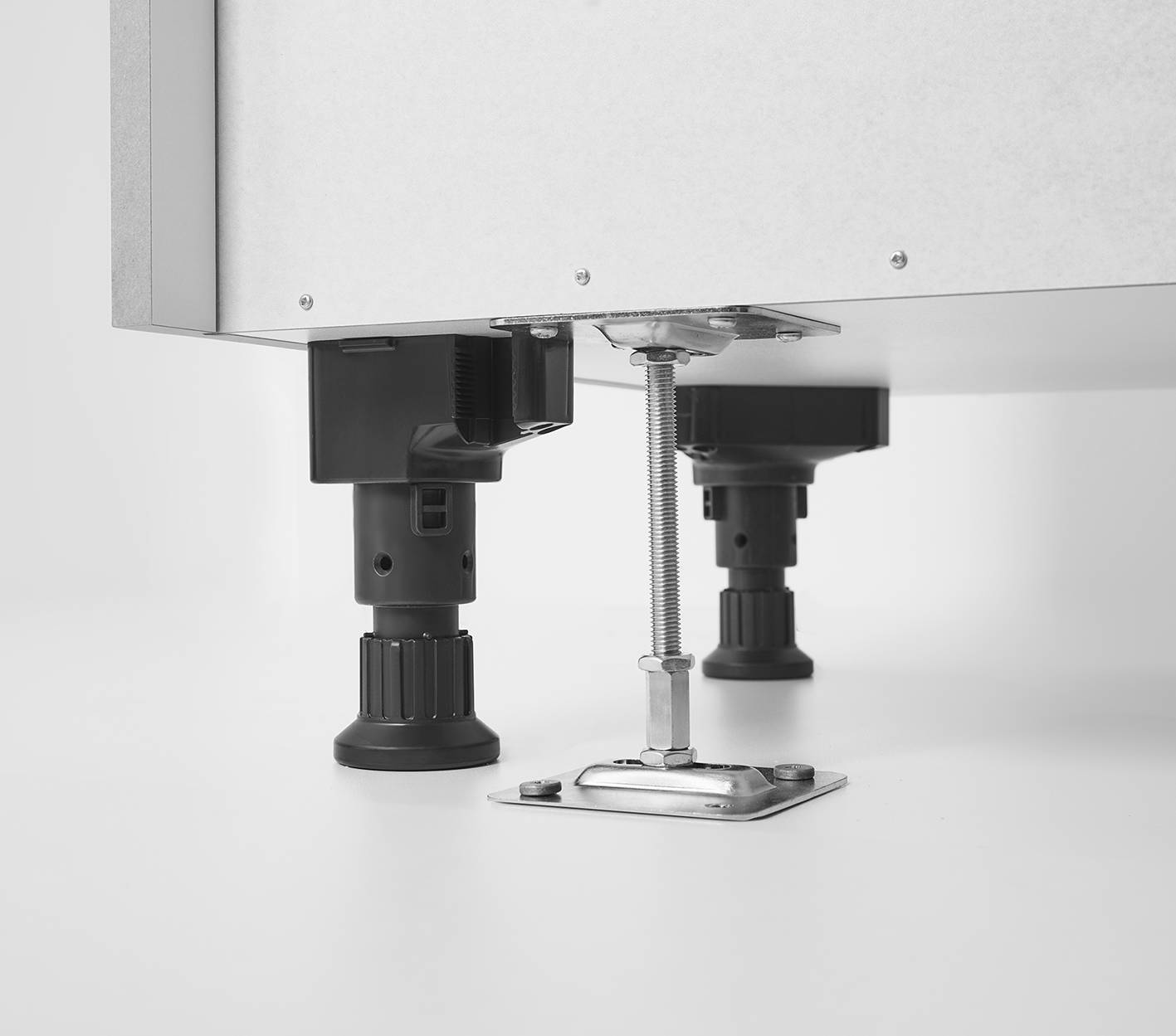 Anti-Tip Cabinet Leg Fixing System — Secure Floor Anchoring for Kitchen Units Close-up product shot on white background showing two adjustable black cabinet legs and a floor-mounted metal anti-tip anchor bracket with a threaded rod, demonstrating the cabinet stabilisation system.