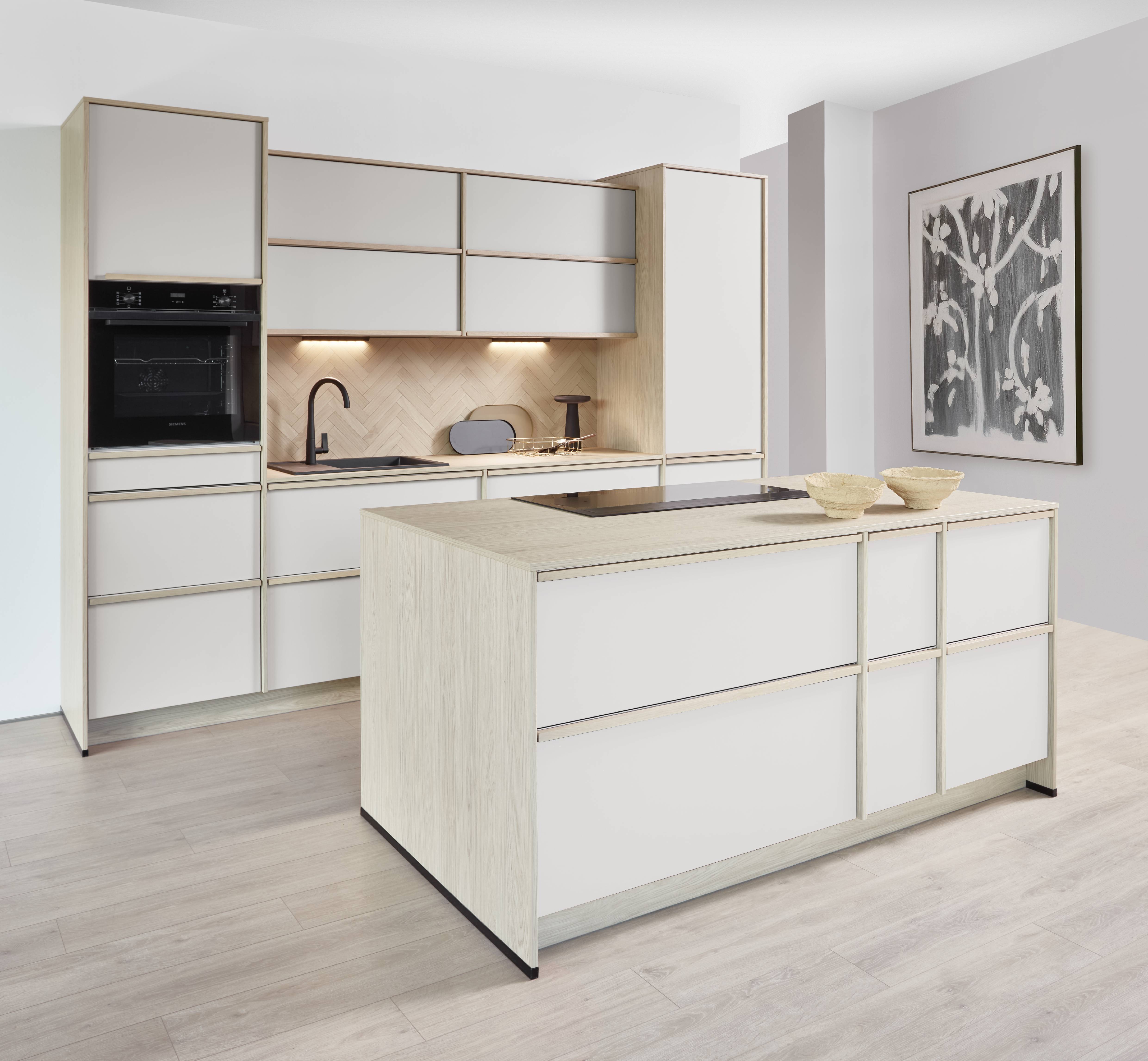 Light, airy, and deceptively storage-rich — this white and oak-framed kitchen uses stacked upper cabinets, a full-depth island with integrated hob, and a herringbone backsplash to make a compact footprint feel anything but small.