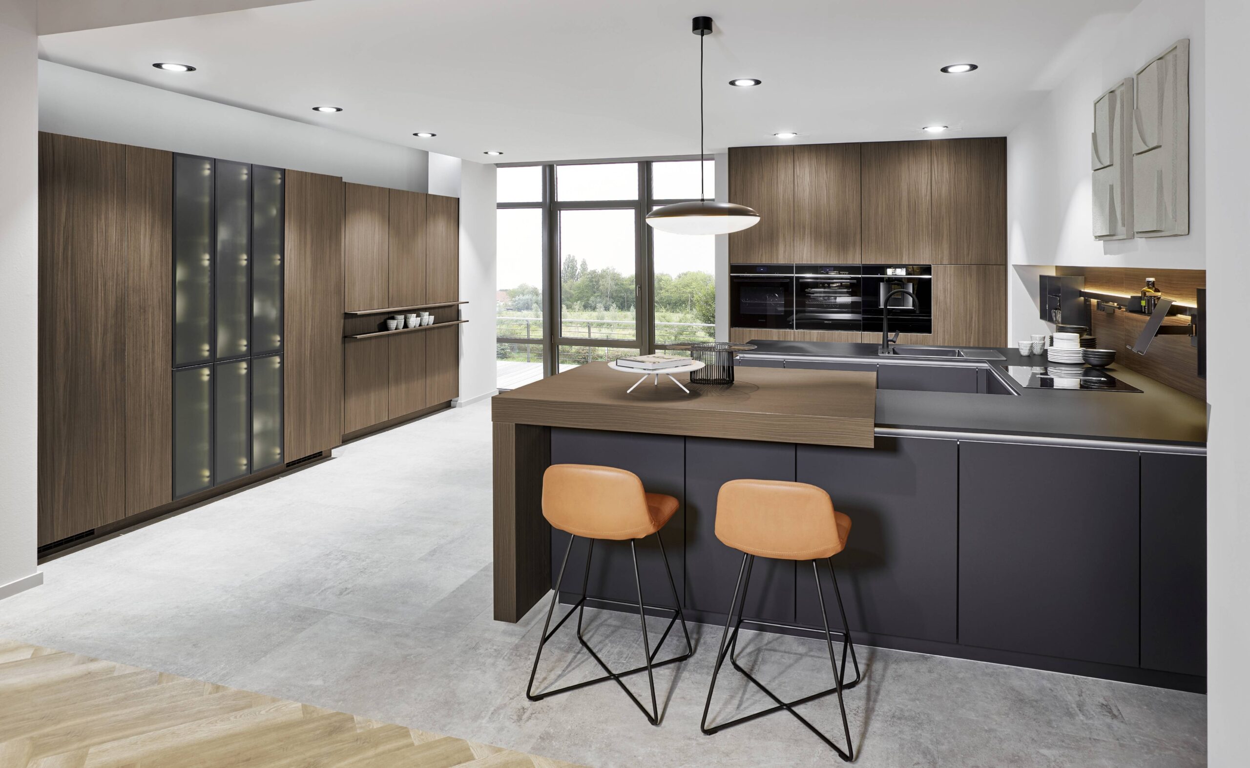 Modular at its most refined — dark smoked oak cabinetry, a graphite island with wood bar extension, and a lit glass display tower show how modular design transforms a home without compromise.