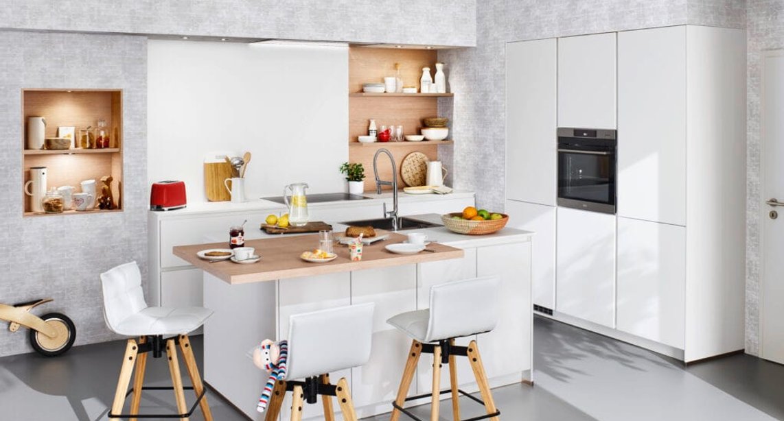 High-end doesn't have to mean cold — this white gloss kitchen pairs sleek cabinetry with warm oak shelving and an inviting island that the whole family gravitates toward.